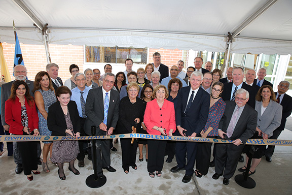 Front row, from left, holding scissors: Yasmin E. Hernandez-Manno, MCC trustee; Blanquita Valenti, freeholder; Ronald Rios, freeholder director; Dorothy K. Power, MCC board chairman; College President Joann La Perla-Morales; Robert Burke, a science major from the class of 1970 who became a pediatrician; Anissa Bousellam ’14; Mark McCormick, MCC’s vice president for academic and student affairs; and Linda Scherr, dean of arts and sciences. They are surrounded by other County and College officials, as well as faculty and staff in the Natural Sciences Department. Classes begin in the building in January.