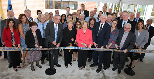 Front row, from left, holding scissors: Yasmin E. Hernandez-Manno, MCC trustee; Blanquita Valenti, freeholder; Ronald Rios, freeholder director; Dorothy K. Power, MCC board chairman; College President Joann La Perla-Morales; Robert Burke, a science major from the class of 1970 who became a pediatrician; Anissa Bousellam ’14; Mark McCormick, MCC’s vice president for academic and student affairs; and Linda Scherr, dean of arts and sciences. They are surrounded by other County and College officials, as well as faculty and staff in the Natural Sciences Department. Classes begin in the building in January. 